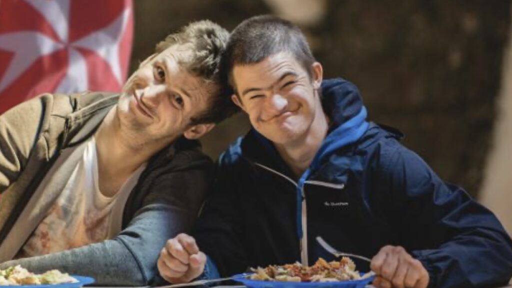 Deux jeunes souriants partageant un repas lors d'une activité de l'Ordre de Malte Belgique
